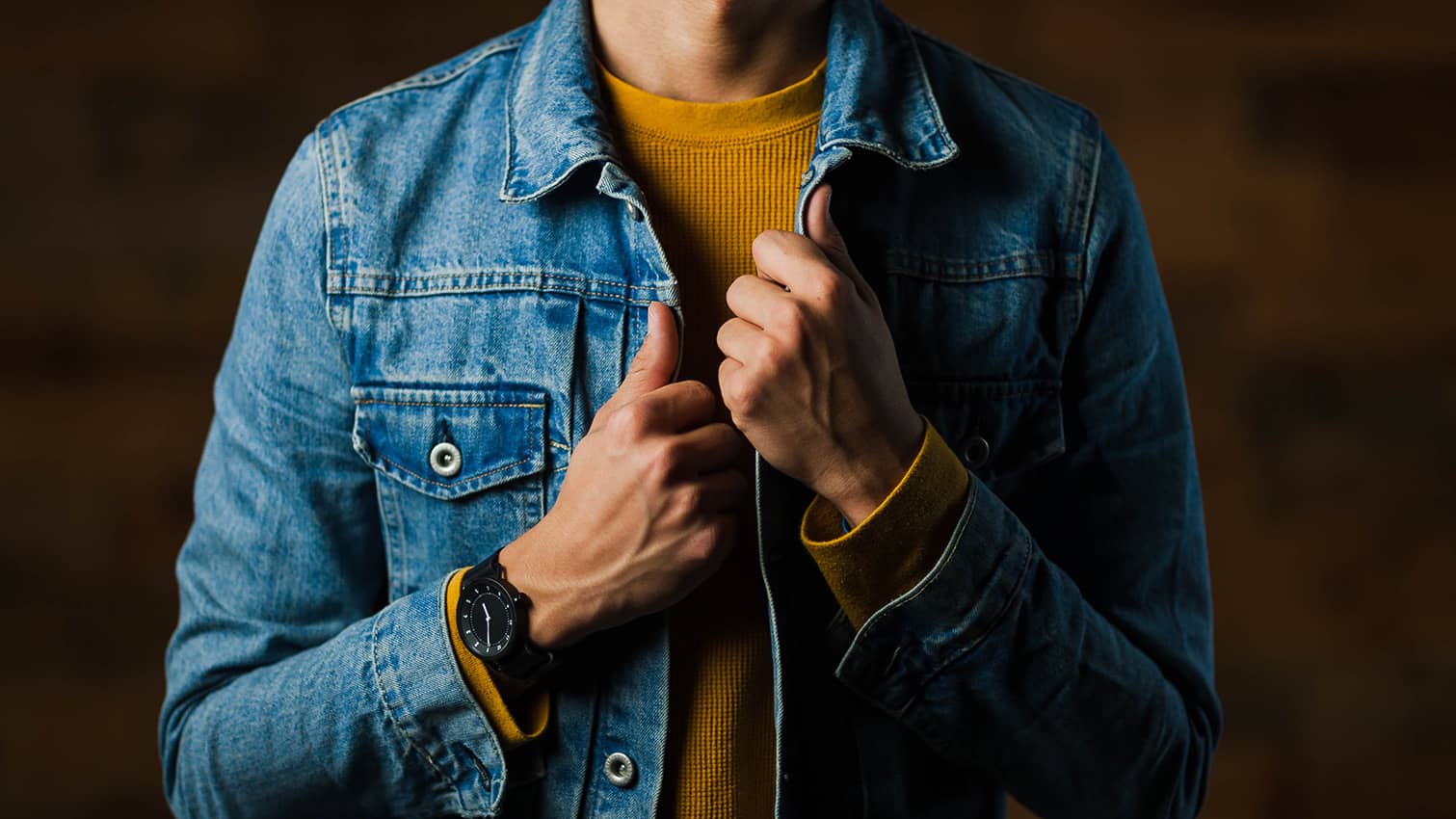 A man wearing a yellow sweater in combination with a denim jacket.
